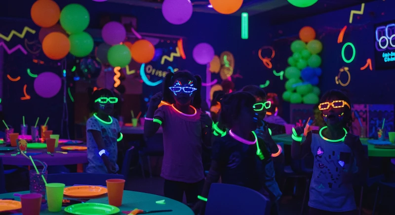 Festa de aniversário infantil com tema neon, inspirada nos anos 80, com luz negra e decoração fluorescente em tons vibrantes, criando um ambiente divertido e imersivo para as crianças.